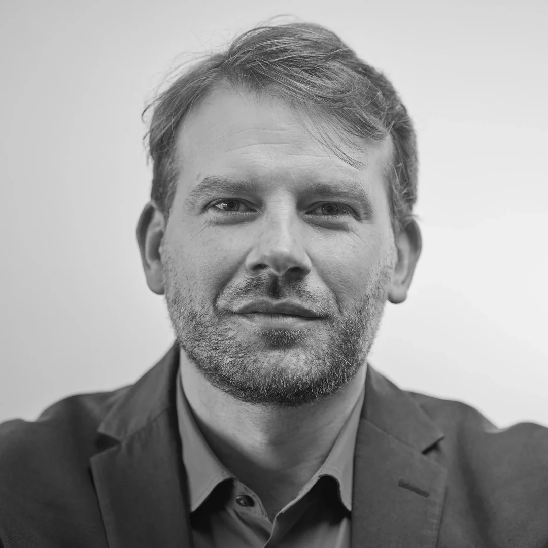 Eine Wissenschaftlerin und ein Wissenschaftler arbeiten hinter einer Glasfassade und mischen Chemikalien mit Großgeräten.