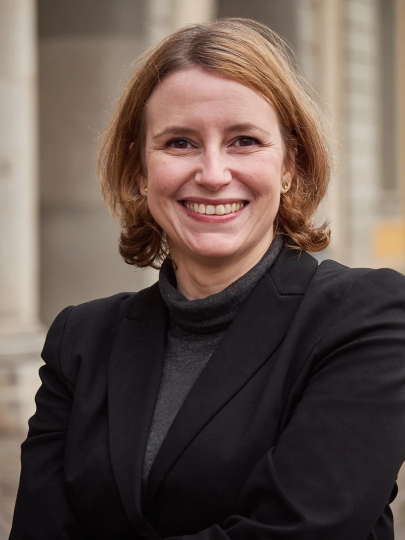 Eine Wissenschaftlerin und ein Wissenschaftler arbeiten hinter einer Glasfassade und mischen Chemikalien mit Großgeräten.